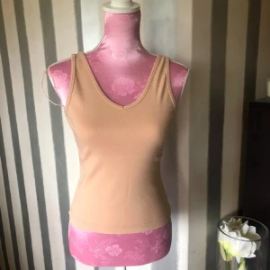 Beige ribbad linnetopp med v-ringning - Snygg beige linnetopp med v-ringning både fram och bak. Toppen är ribbad och har en tight passform som framhäver siluetten. Perfekt att styla med jeans eller kjol för en clean och enkel look.