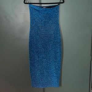 Blå glittrig klänning Gina Tricot - Supersnygg blå glittrig klänning från Gina Tricot. Klänningen är figurnära med slits bak och har en glittrig yta som verkligen sticker ut. Perfekt för dig som vill glänsa och synas. Materialet är stretchigt och bekvämt. Aldrig använd, endast testat men tagit bort prislapp.