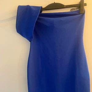 Kornblå one shoulder kortklänning - Snygg kornblå kortklänning med one shoulder-design. Klänningen har en figurnära passform och är tillverkad i ett slätt, stretchigt material. Perfekt för dig som vill sticka ut med en cool och modern look. Har enbart använts en gång. Storleken är M men passar även för S.