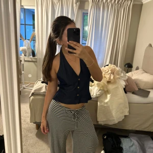 Mörkblå omlottväst med knappar - Snygg mörkblå väst med halterneck och djup v-ringning. Västen har knappar framtill och knytning i ryggen för en tight passform. Croppad modell som ger en modern och trendig look. Perfekt att styla med jeans eller kjol.