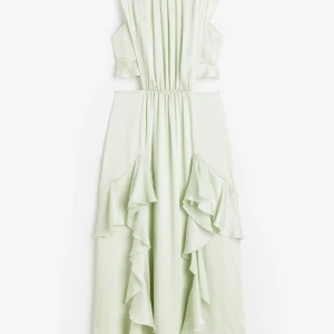 Ljusgrön långklänning med volanger - Superfin ljusgrön långklänning med volangdetaljer och cut-outs i midjan. Klänningen har en flowy passform och är ärmlös, perfekt för sommarens alla tillfällen. Materialet känns lätt och luftigt, vilket gör den extra bekväm och snygg.