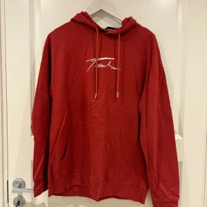 Röd och grå hoodie från Trend - Två hoodies från Trend, en i rött och en i grått, båda med vit broderad logga på bröstet. Klassisk känguruficka, huva med snörning och lång ärm. Perfekt för chill dagar eller när du vill ha en enkel men snygg stil.