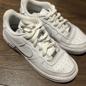 Nike Air Force 1 vita sneakers - Använda endast några gånger. Klassiska Nike Air Force 1 sneakers i helvitt skinn med perforerad tå, rund tå och platt sula. Snygg och tidlös modell med snörning och ikonisk Swoosh-logga på sidan. Perfekta för dig som gillar en clean och sportig look.                  Inköpspris 1080 kr. 