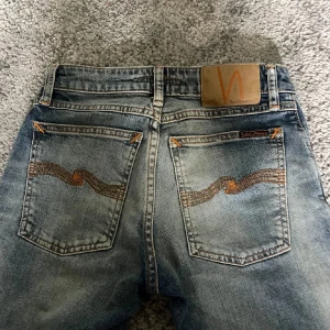 Nudie Jeans slim ljusblå 25/28 - Snygga skinny jeans från Nudie Jeans i ljusblå tvätt med slitningar och klassiska orange sömmar på bakfickorna. Modellen har normal midja och slim vid benen men sitter riktigt skönt. Perfekta för dig som gillar en smal passform och stilren look. Priset kan diskuteras!