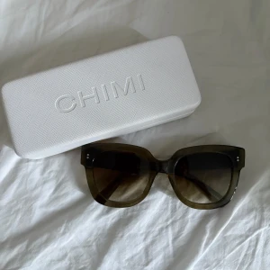 solglasögon från chimi - Snygga solglasögon från chimi med fyrkantig form. Glasen är bruna med en snygg toning. Perfekt accessoar för att lyfta din stil och skydda ögonen mot solen. Kommer med ett stilrent vitt fodral.
