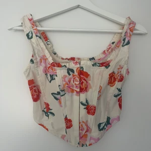 Blommig korsettopp från Stradivarius - Korsettopp från Stradivarius i vit med stora blommor i rosa, rött och orange. 
