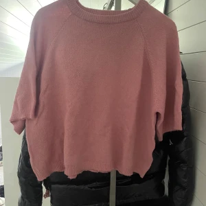 Rosa stickad tröja från 157 - Mysig rosa stickad tröja från 157 med rund halsringning och kortare ärmar. Tröjan har en loose passform och ribbade muddar vid hals, ärmslut och nederkant. Perfekt för dig som gillar en chill och enkel stil.