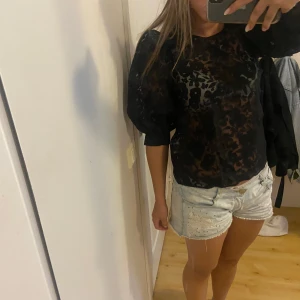 Svart transparent blus med puffärm - Snygg svart blus från Sisters Point med transparent tyg och diskret blommönster. Blusen har puffiga långärmar och rund halsringning, perfekt för dig som vill sticka ut lite extra. Lätt och luftig känsla, passar till både jeans och kjol.