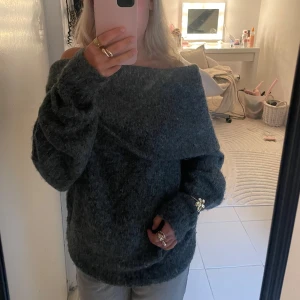 Mörkgrå offshoulder stickad tröja - Supermjuk  mörkgrå stickad tröja med bred offshoulder-krage. Långärmad modell med avslappnad passform och ribbade muddar. Snygg att styla med jeans. Den känns väldigt tjock och dyr i materialet. Helt oanvänd! 