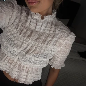Vit volangig blus med kort ärm - Supersöt vit blus med volanger. Tunt, lätt material som ger en luftig känsla. Lite genomskinlig 🤍 passar Xs/S