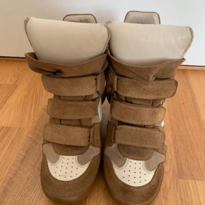 Isabel Marant wedge sneakers beige/brun - Coola Isabel Marant sneakers med kilklack i beige och brunt mocka och skinn. Skorna har flera kardborreband, rund tå och perforerade detaljer framtill. Perfekta för dig som vill ha en sportig men ändå trendig look.