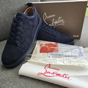 Mörkblå sneakers från Christian Louboutin - Exklusiva mörkblå sneakers från Christian Louboutin i mocka med klassisk röd sula och snygga ton-i-ton snören. Skorna har rund tå, platt sula och lyxig läderinsida. Perfekta för dig som vill sticka ut med stilrena detaljer och premiumkänsla.
