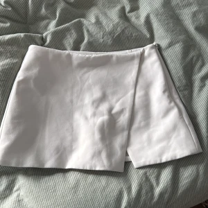 Vit omlottkjol från Zara - Säljer en stilren vit kortkjol från Zara i omlottmodell med shorts under 