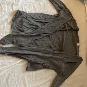Grå kofta från H&M Basic, storlek S - En tunn och mjuk grå kofta från H&M Basic i storlek S. Koftan har lång ärm och öppen framtill utan knappar, perfekt att slänga på sig över en t-shirt eller linne. Enkel och stilren design som funkar till det mesta.