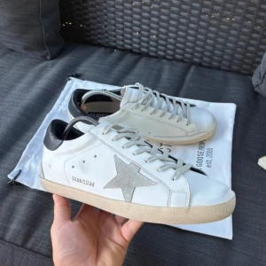 Golden Goose sneakers  - Snygga vita sneakers från Golden Goose med grå mockadetaljer och en ikonisk stjärna på sidan. Skorna är väl omhändertagna o endast använt ett fåtal gånger. OG dustbag och Kvitto finns. Vid fler funderingar är det bara att höra av sig så hjälper vi er så gott vi kan. 🍻