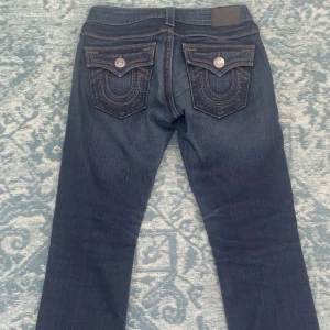 True Religion jeans - Vintage mörkblå jeans från True Religion, extremt lågmidjade med bakfickor och kontrastsömmar. Modellen har normal passform och raka ben och silverfärgade knappar. Som referens är jag 160 cm. Nypris 1100 kr. Kan mötas upp i Stockholm!