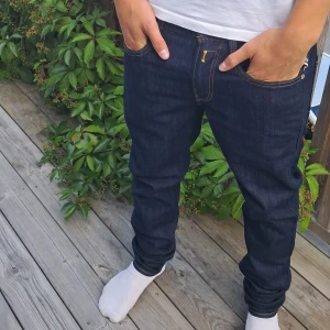 Replay Anbass mörkblå jeans slim fit - Snygga mörkblå Replay Anbass jeans i slim fit med klassiska kontrastsömmar och detaljer som myntficka med dragkedja. Jeansen har raka ben och är tillverkade i slitstarkt denim med läderpatch bak. Perfekta för dig som gillar stilrena och moderna jeans. W29 L32