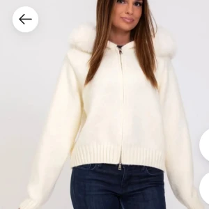 Vit stickad hoodie med fuskpäls - Supermysig vit stickad hoodie med dragkedja och fluffig fuskpäls runt huvan. Tröjan har ribbade muddar och är croppad i modellen, perfekt för lager på lager. Långärmad och riktigt cozy vibe.