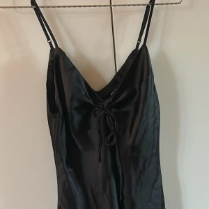 Svart satin klänning - Supersnygg svart kort klänning från Bik Bok i satin material. Aldrig använd, prislappen är kvar! Klänningen har smala axelband, v-ringning och en snygg snörningsdetalj framtill. Den är för stor för mig så därför har jag inga bilder på mig i den. 