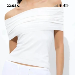 Vit offshoulder topp - Snygg vit offshoulder topp med draperad kant över axlarna. Toppens passform är figurnära och den är ärmlös, perfekt för en fräsch och stilren look. Enkel att matcha med både jeans och kjol.