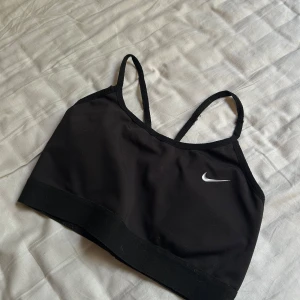 🫶🏻 - Säljer en svart linnetopp från Nike med smala axelband som korsas i ryggen. Toppen har en enkel och sportig design med Nike-loggan i vitt framtill. Perfekt för träning eller chill dagar. Materialet är mjukt och stretchigt för bästa komfort.