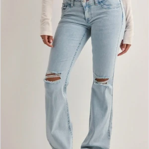 Ljusblå bootcut jeans med slitningar från Nelly  - Snygga ljusblå jeans med bootcut passform och slitna hål över knäna. Jeansen har lågmidja och coola broderade detaljer på bakfickorna. Perfekta för en avslappnad och trendig look. Nypris 699. Använda 3 gånger 