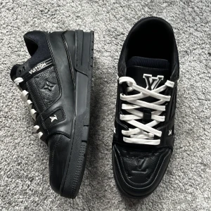 Louis Vuitton svarta sneakers  - Exklusiva svarta Louis Vuitton sneakers i skinn med vita snören och tydliga LV-loggor på plös och sula. Snygg chunky sula och detaljerad präglad logotyp på sidan. Tillverkade i Italien, perfekt för dig som vill sticka ut med lyxig streetstyle. Ingen box ingår.