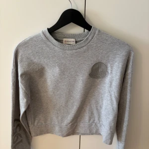 Moncler tröja - Moncler Enfant “Completo maglia girocollo” sweatshirt i mycket bra skick. Grå, lätt cropped modell med ton-i-ton logga på bröstet och tryck ”1952” på ärmen. Köpt på NK Kids som en del av ett set. Äkthetsmärkning med QR-kod finns (kan visas vid köp). Storleken syns tyvärr inte på tröjan (detta var ett set där storleken ofta bara stod på byxorna), men motsvarar ca xs-s  Nypris för set ca 6 000 kr. Mitt pris: 2 200 kr.