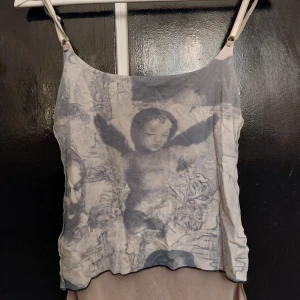 Ärmlös linnetopp med ängelmotiv - Fin ärmlös linnetopp med tunna axelband me ängelmotiv i grått och vitt. Toppen har en lätt transparent känsla och ett coolt print, kan användas på båda hållen