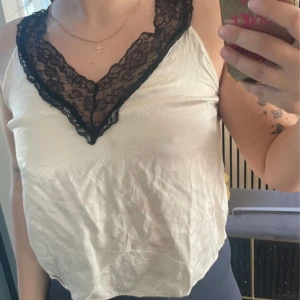 Vit linnetopp med svart spets - Säljer en snygg vit linnetopp med breda axelband och djup v-ringning dekorerad med svart spets. Tröjan är väldigt skön och fin, har använt den några gånger🤍