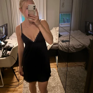 Marinblå kort klänning med spetsdetaljer - Supersöt marinblå kort klänning med tunna axelband och v-ringning. Spetsdetaljer längs urringning och fåll ger en extra touch. Perfekt för dig som gillar en enkel men ändå elegant stil.