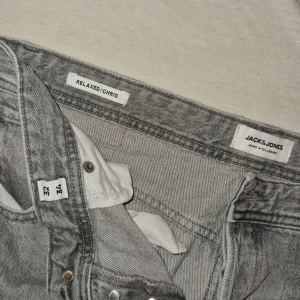 Gråa relaxed jeans från Jack & Jones - Säljer ett par gråa relaxed fit jeans från Jack & Jones, modell Relaxed Chris. Jeansen har klassisk femficksdesign, raka ben och knäppning med knappar. Perfekta om du gillar en lite lösare och chill stil. Materialet är klassisk denim i bomull.