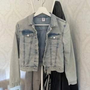 Ljusblå jeansjacka från &Denim - Snygg ljusblå jeansjacka från &Denim med klassisk krage, två bröstfickor med knappar och slitna detaljer. Jackan har en croppad passform och långa ärmar, perfekt att slänga över en hoodie eller t-shirt för en chill look.