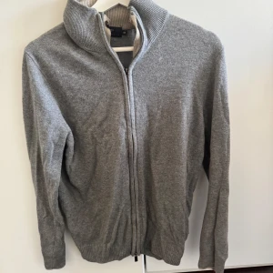 Grå kashmirkofta från Libero Milano - Snygg grå kofta i mjuk kashmir från Libero Milano. Koftan har ribbad krage, hel dragkedja framtill och långa ärmar. Perfekt för dig som gillar stilrena och bekväma plagg med exklusiv känsla. Passar till jeans eller chinos för en chill look. storlek 48=S/M