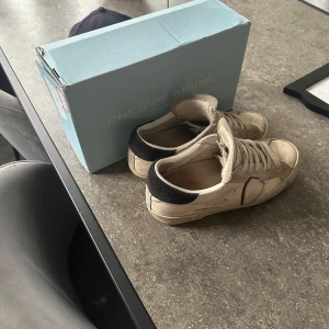 Vita sneakers från Philippe Model  - Snygga vita sneakers från Philippe Model med mörkblå häl och logotyp på sidan. Skorna har snörning och är tillverkade i skinn och mocka. Perfekta för dig som gillar stilrena och klassiska sneakers med en twist.  Skriv vid intresse och pris kan diskuteras.