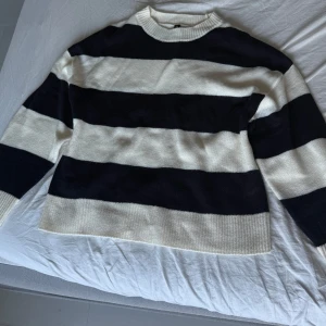 Randig stickad tröja från H&M - Säljer en stickad tröja från H&M i storlek S med breda svarta och vita ränder. Tröjan har rund halsringning och långa ärmar, perfekt för lager-på-lager under kyliga dagar. Klassisk och enkel stil som funkar till det mesta.