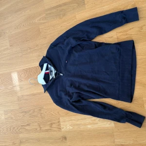 Marinblå half zip från Tommy Hilfiger S - Snygg marinblå långärmad tröja från Tommy Hilfiger i premium bomull. Tröjan har half zip-dragkedja, ribbade muddar och diskret logga på bröstet. Kragen har coola rödvita detaljer som ger en sportig vibe. Strl S köpt för 749kr mitt pris 399kr.