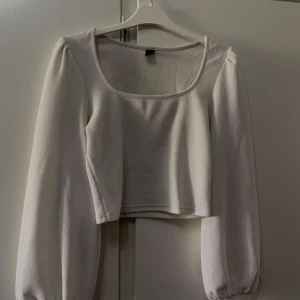 Vit croppad långärmad topp - Snygg vit croppad topp med långa puffärmar och fyrkantig ringning. Perfekt för att styla med höga jeans eller kjol. Toppens material känns mjukt och bekvämt mot huden.