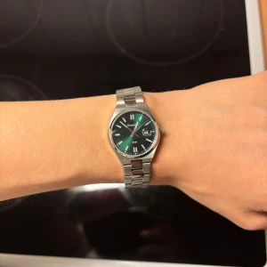 Grön klocka med silverlänk - Stilren klocka med grön urtavla och datumvisning. Klockan har en klassisk rund form och en robust länk i silverfärgad metall. Perfekt accessoar för dig som vill sticka ut med en elegant detalj.