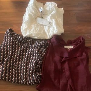 Tre snygga blusar i olika stilar - Paket med tre blusar: en vit blus från Y.A.S i lätt, krispigt tyg, en vinröd blus från Flash Woman med knytdetalj vid halsen och en mönstrad blus i brunt, rosa och vitt med grafiskt mönster. Perfekt för dig som gillar att variera din stil!