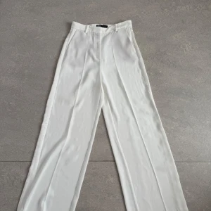 Vita wide kostymbyxor från Zara - Snygga vita kostymbyxor från Zara i storlek S. Byxorna har hög midja, raka och vida ben. Köpta secondhand, aldrig använda av mig. Felfria!