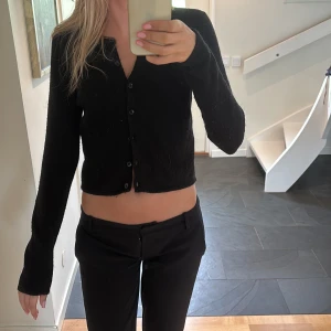 Svart kofta med knappar - Säljer en svart kofta med långa ärmar och knäppning framtill. Enkel och stilren design som passar perfekt till både jeans och kostymbyxor. Mjuk och skön, perfekt för lager-på-lager under kyligare dagar.