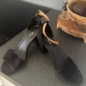 Svarta sandaler med klack - Stilrena svarta sandaler från Alley med bred rem över tårna och öppen tå. Skorna har en chunky klack och en beige rem runt hälen som ger en snygg kontrast. Perfekta för att lyfta din outfit med en enkel men trendig look.