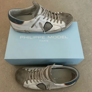 Philippe Model skor - Säljer ett par snygga Philippe Model sneakers i vitt med grå detaljer och blå häl och orange sula under. Skorna är i ett bra skick och ser bra ut om man vill va lite extra grish. Pris kan alltid diskuteras de är bara att höra av sig (Riktiga)