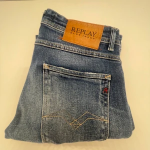 Replay Willbi blå slim jeans - Snygga blå jeans från Replay, modell Willbi med regular slim fit. Jeansen har slitna detaljer framtill, klassisk femficksdesign och läderpatch med Replay-logga bak. Perfekta för dig som gillar en smalare passform och cool tvätt. En slitning/hål på knät kan skicka bild om du vill se. 