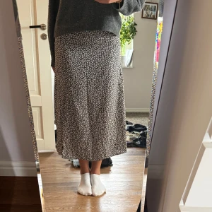 Svart blommig långkjol  - Supersöt svart långkjol med vita och gula blommor. Kjolen har ett mjukt och följsamt tyg som känns skönt mot huden. Perfekt för dig som gillar somriga mönster och vill ha en flowy look.