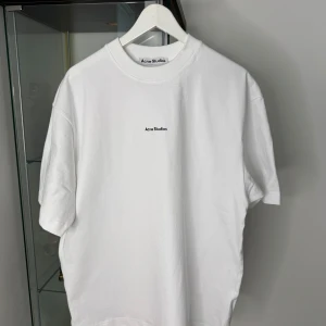 Vit t-shirt från Acne Studios - Clean vit t-shirt från Acne Studios i 100% bomull. Klassisk passform med korta ärmar och rund halsringning. Diskret Acne Studios-logga tryckt på bröstet. Perfekt basic-plagg för en stilren look.