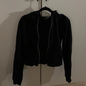 Svart hoodie med dragkedja från H&M Divided - Svart hoodie från H&M Divided i storlek XS. Tröjan har huva, långa ärmar och en hel dragkedja framtill. 