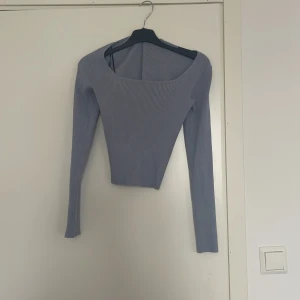 Ljusblå ribbad långärmad topp - Säljer en ljusblå ribbad topp med lång ärm och croppad passform. Toppen har en bred, rundad urringning och är tillverkad i ett stretchigt matrial.