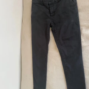 Svarta byxor  - Svarta byxor från Pier One med smal passform och klassisk design. Byxorna har normal midja, bälteshällor och är tillverkade i bomullsmix som känns mjuk och följsam. Perfekta för en clean och stilren look.